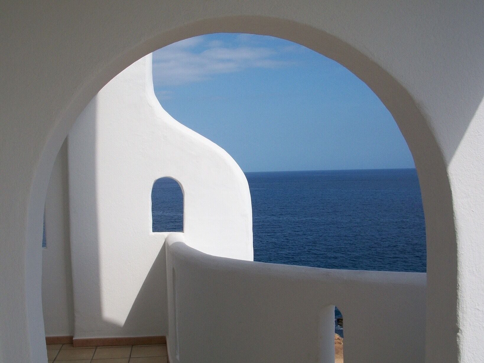 A white building with an arched doorway overlooking the sea.