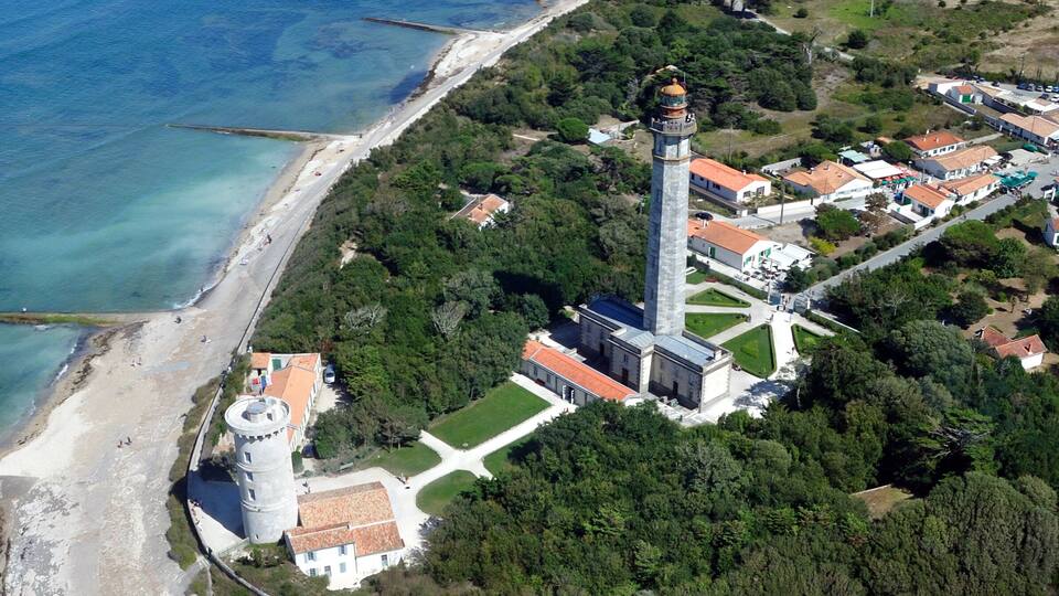 An aerial view of a coastal area with a lighthouse, beach, and surrounding greenery.