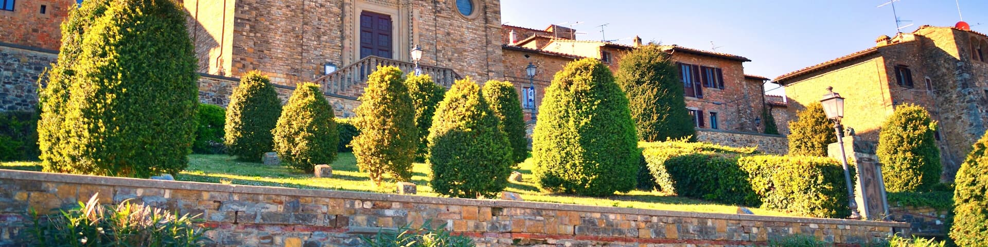 A historic stone church with a bell tower, surrounded by well-maintained hedges and a stone wall.