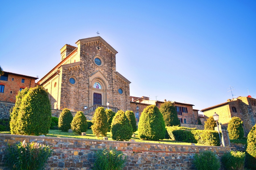 Un'antica chiesa in pietra con un campanile, circondata da siepi curate e un muro in pietra.