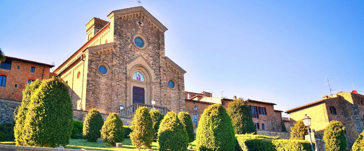 A historic stone church with a bell tower, surrounded by well-maintained hedges and a stone wall.
