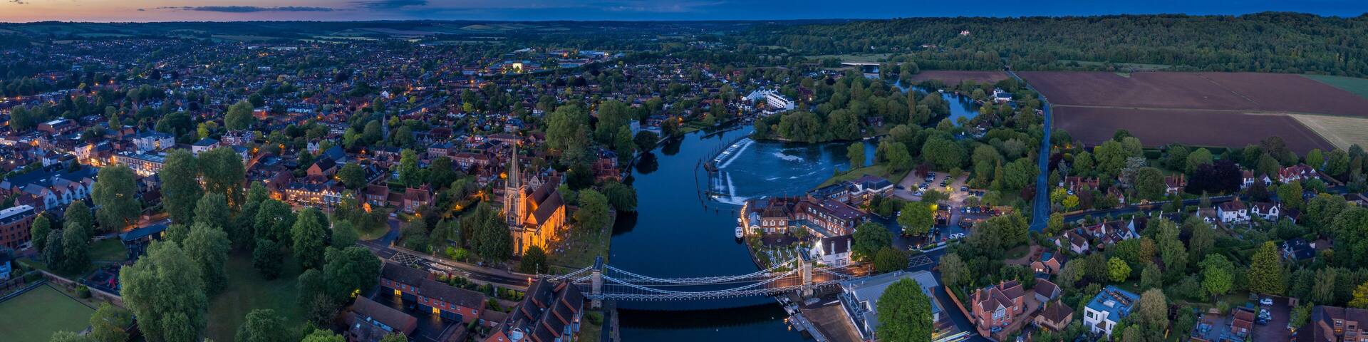 An aerial view of a town with a river, a bridge, and surrounding greenery.
