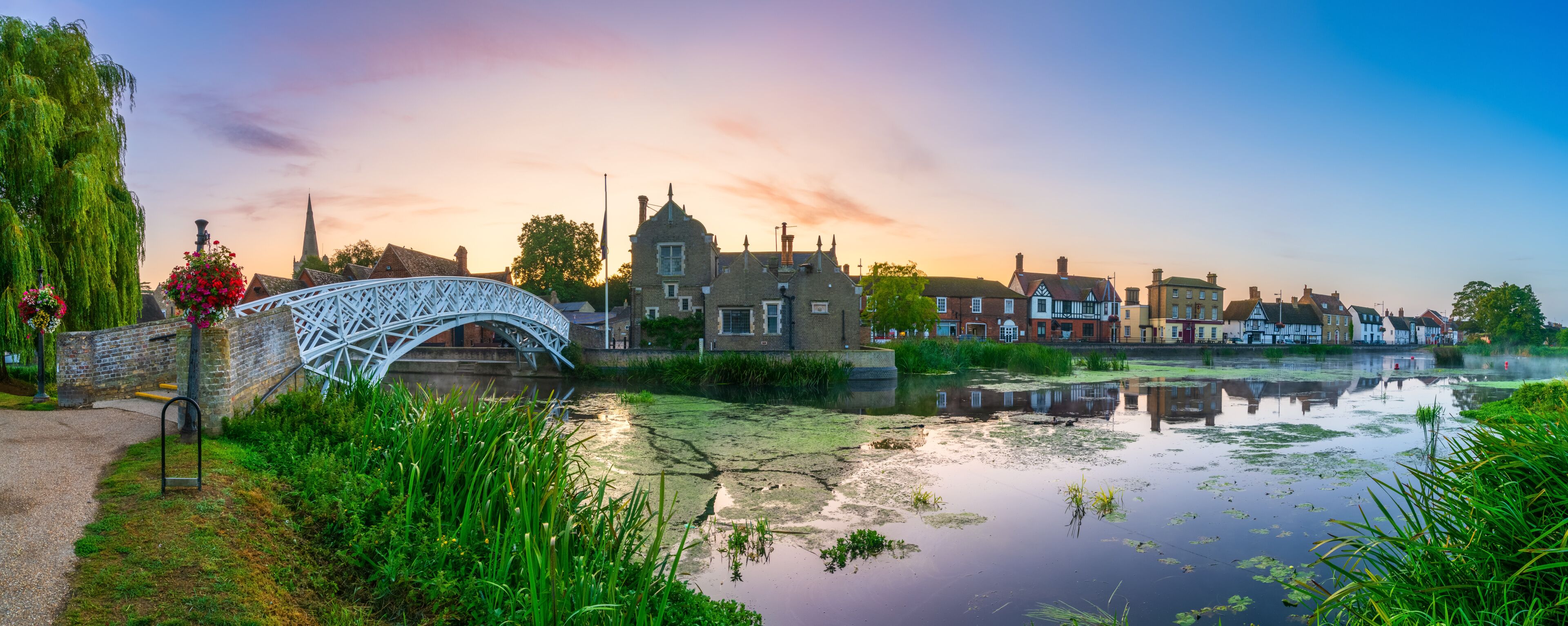 A historic bridge, a river, and traditional buildings during sunset.