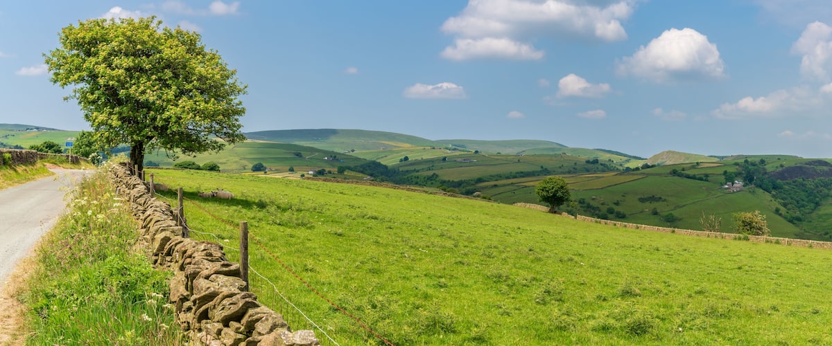 A stone wall, a narrow road, and rolling green hills under a clear sky.