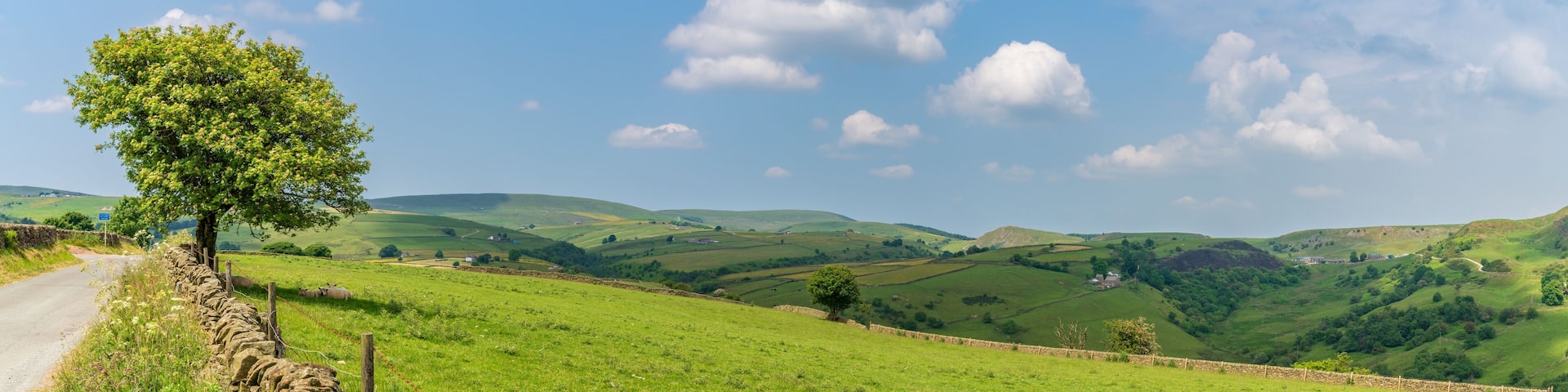 A stone wall, a narrow road, and rolling green hills under a clear sky.