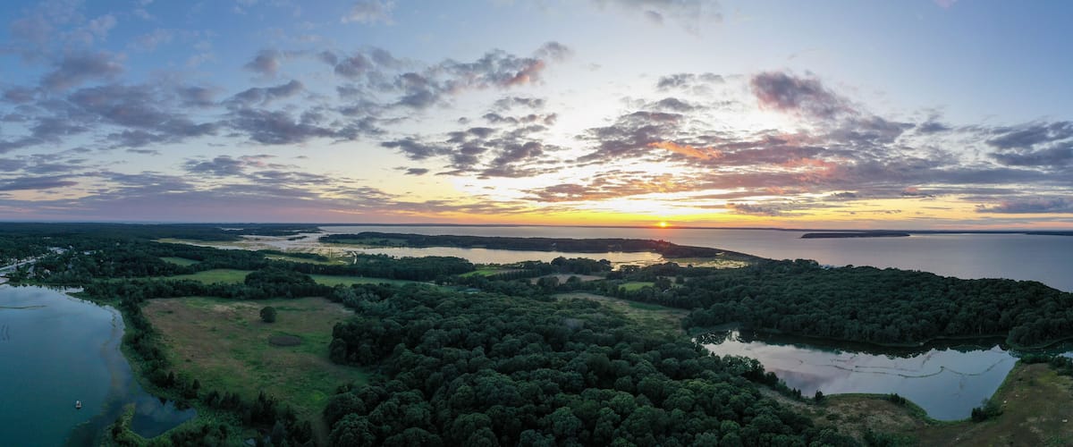 A sunset over a lake surrounded by dense forests and a distant shoreline.