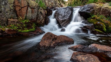 Uma cascata descendo sobre rochas em uma área arborizada.