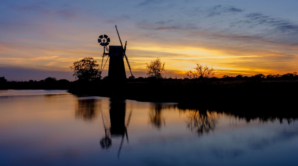 A sunset over a calm body of water with a tower structure silhouetted against the sky.