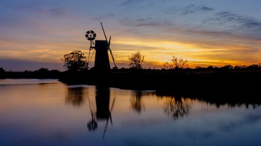 A sunset over a calm body of water with a tower structure silhouetted against the sky.