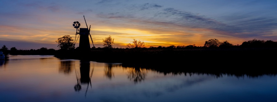 Solnedgang over rolige vandflader med en tårnstruktur silhouetteret mod himlen.