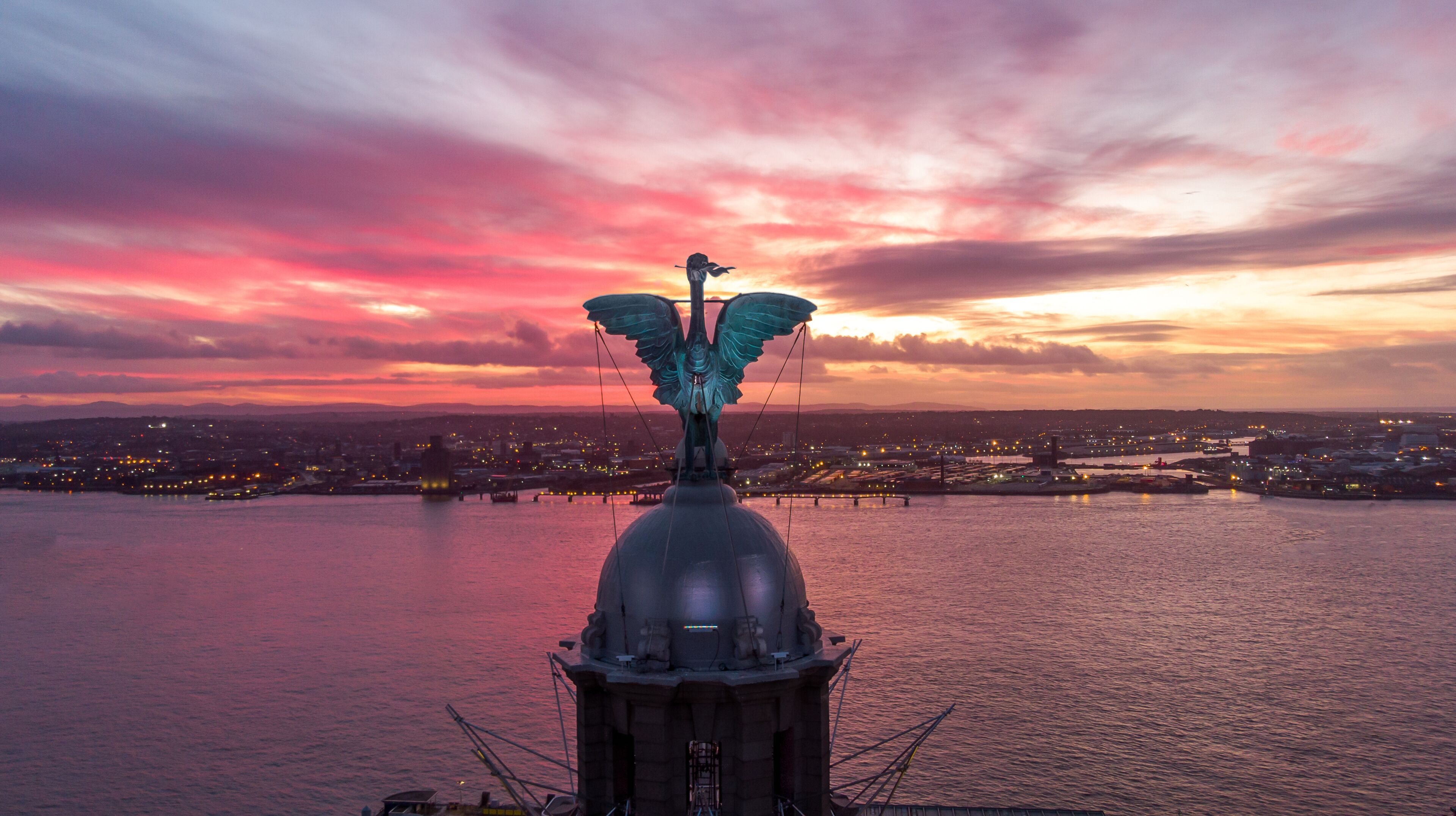 A statue of an angel with wings on a dome, overlooking a cityscape at sunset.