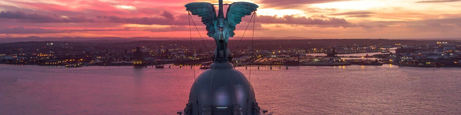 A statue of an angel with wings on a dome, overlooking a cityscape at sunset.