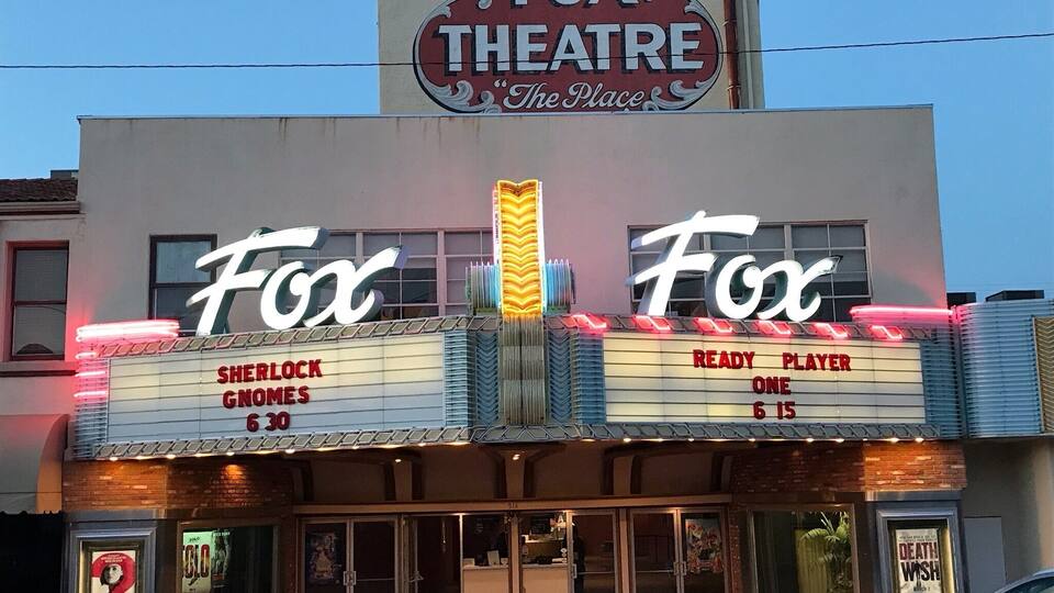 A theater with a marquee reading "FOX THEATRE The Place" and movie titles "SHERLOCK GNORES" and "READY PLAYER ONE".