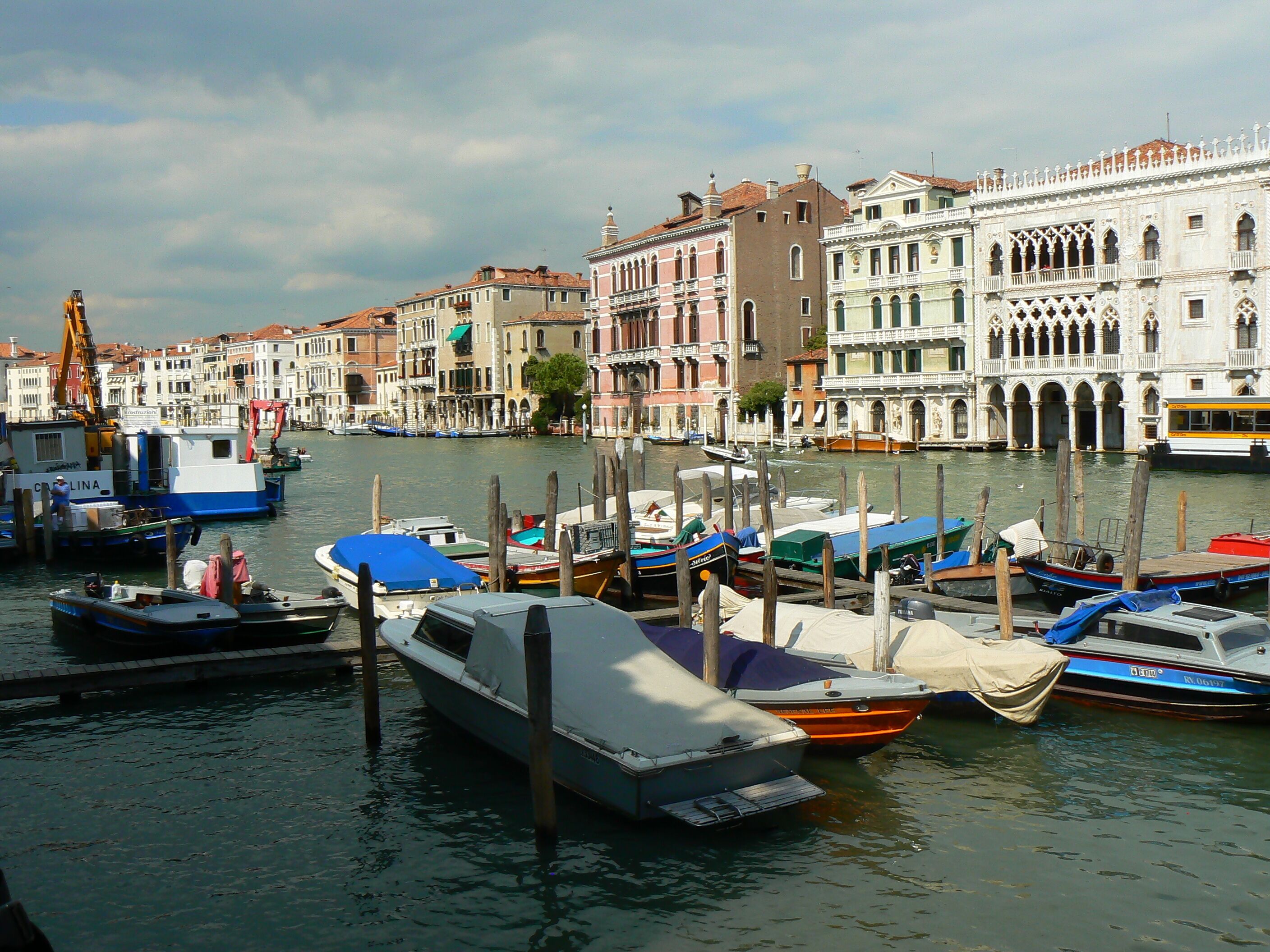 A canal with boats docked, historic buildings, and a yellow bus.