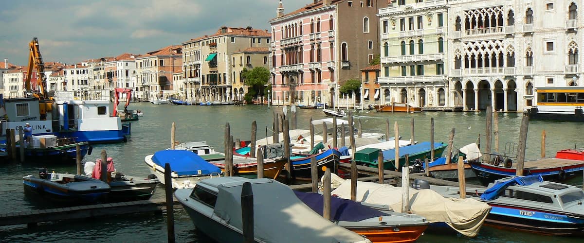 A canal with boats docked, historic buildings, and a yellow bus.