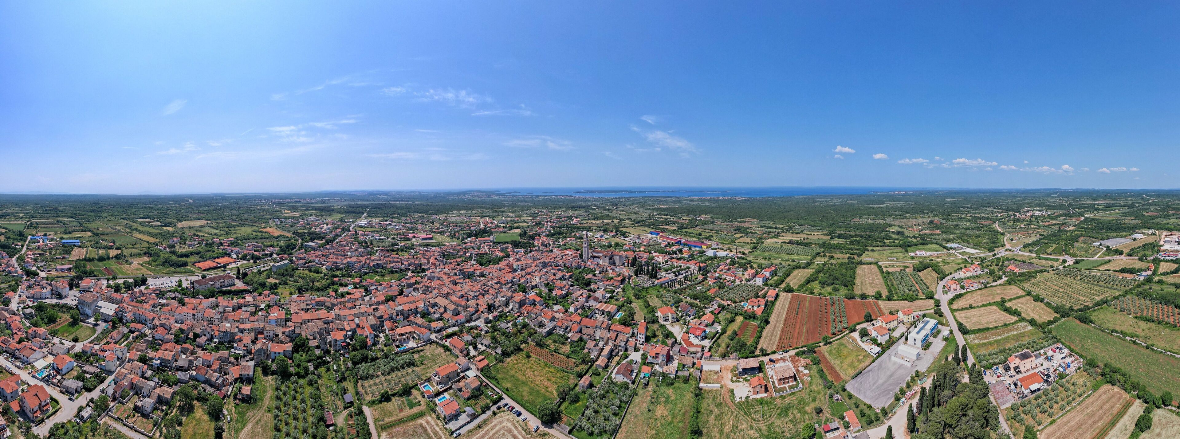 An aerial view of a town with red-roofed houses, green fields, and a clear blue sky.