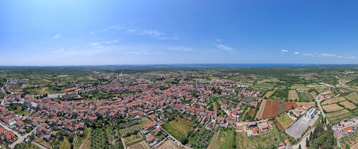 An aerial view of a town with red-roofed houses, green fields, and a clear blue sky.