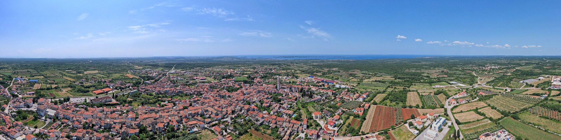 An aerial view of a town with red-roofed houses, green fields, and a clear blue sky.