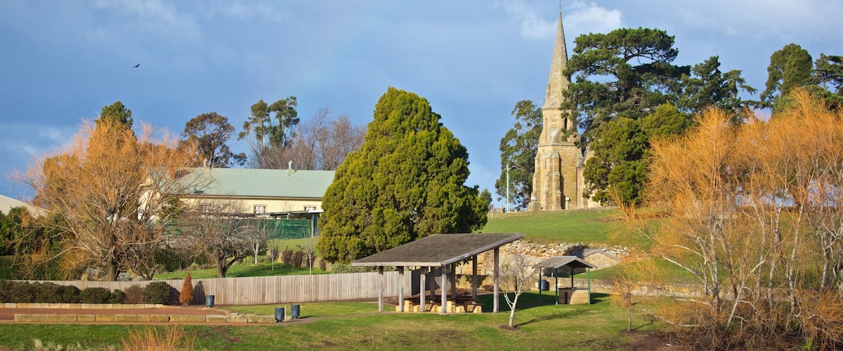 A park with a pond, picnic shelter, a church steeple, and autumn trees.