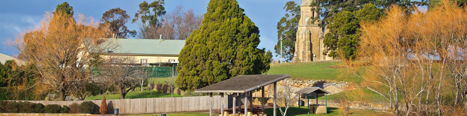 A park with a pond, picnic shelter, a church steeple, and autumn trees.