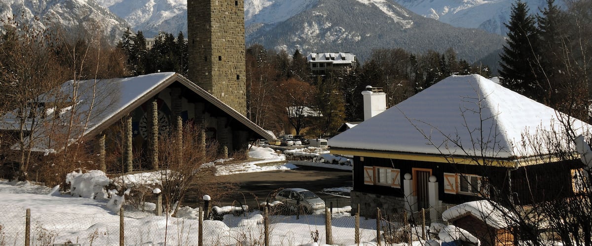 A church with a bell tower, surrounded by snow-covered mountains and trees.