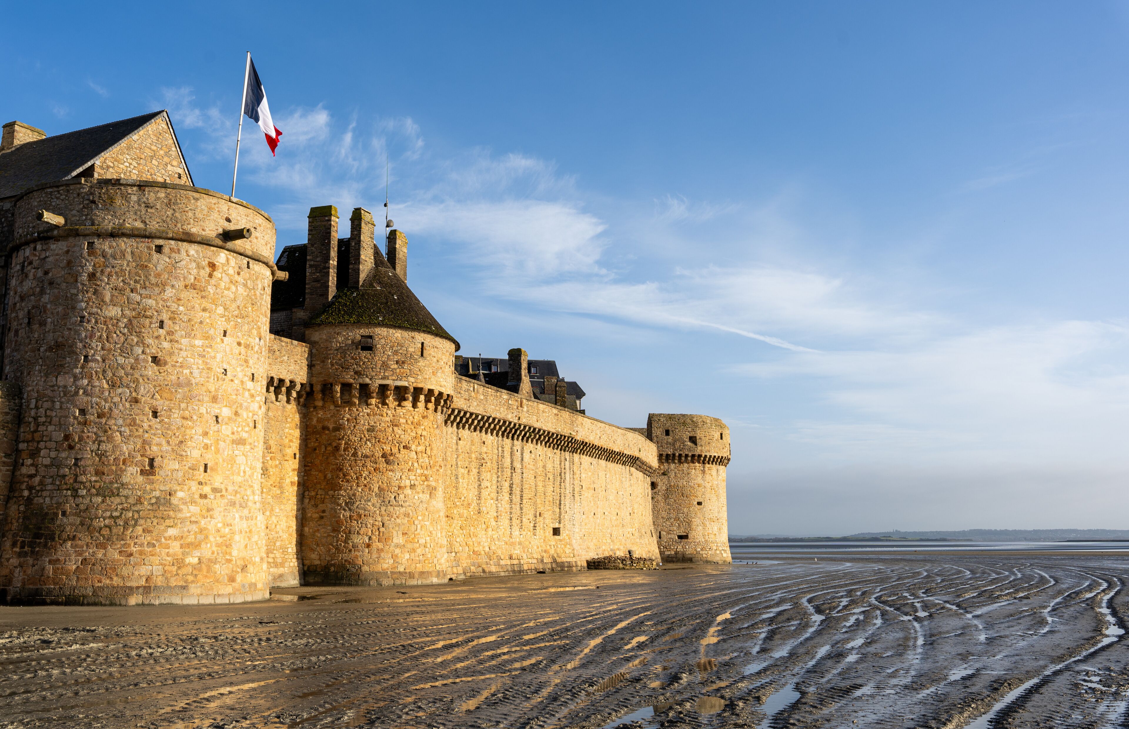 Um castelo de pedra histórico com uma bandeira, um fosso e um céu limpo.