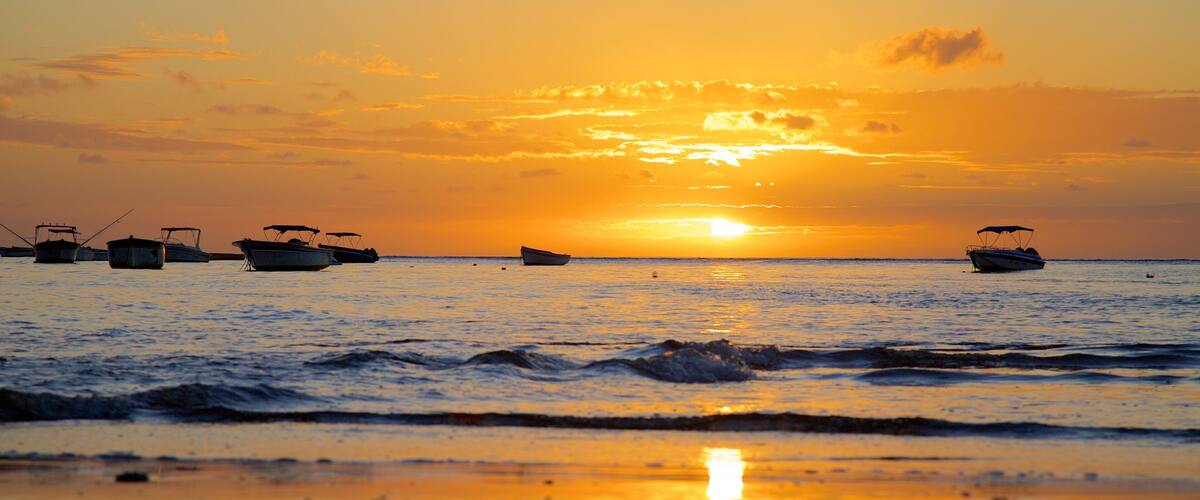 A sunset over a calm sea with several boats anchored.