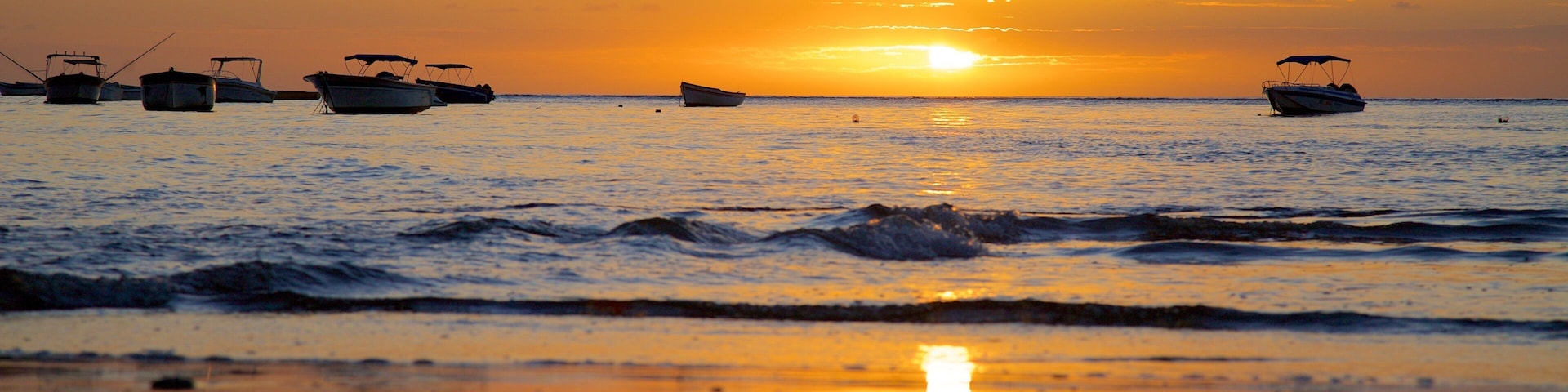 A sunset over a calm sea with several boats anchored.