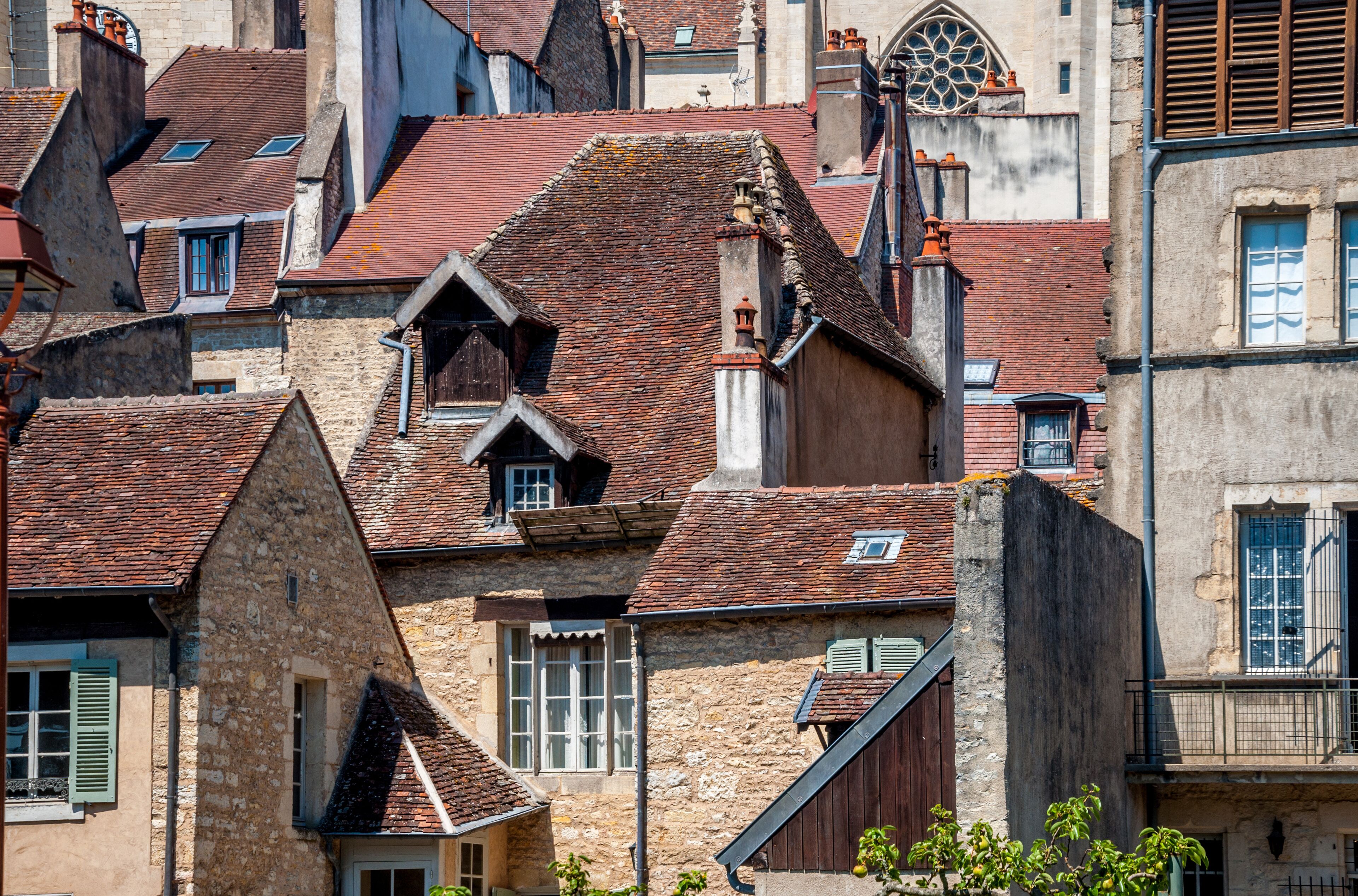 A historic European town with stone buildings, red-tiled roofs, and a prominent church with a large rose window.