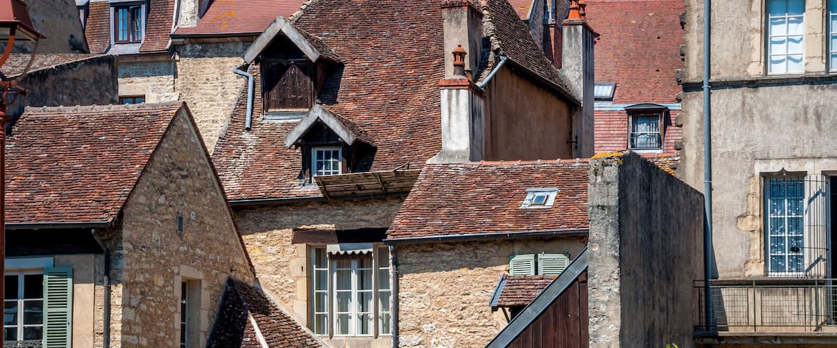 A historic European town with stone buildings, red-tiled roofs, and a prominent church with a large rose window.