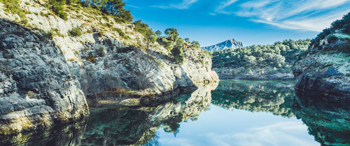 A calm lake reflecting rocky cliffs and trees.