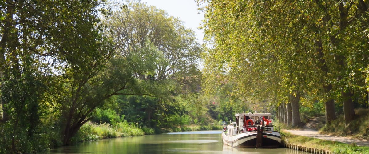 A narrow waterway flanked by dense green foliage, with a boat anchored in the middle.