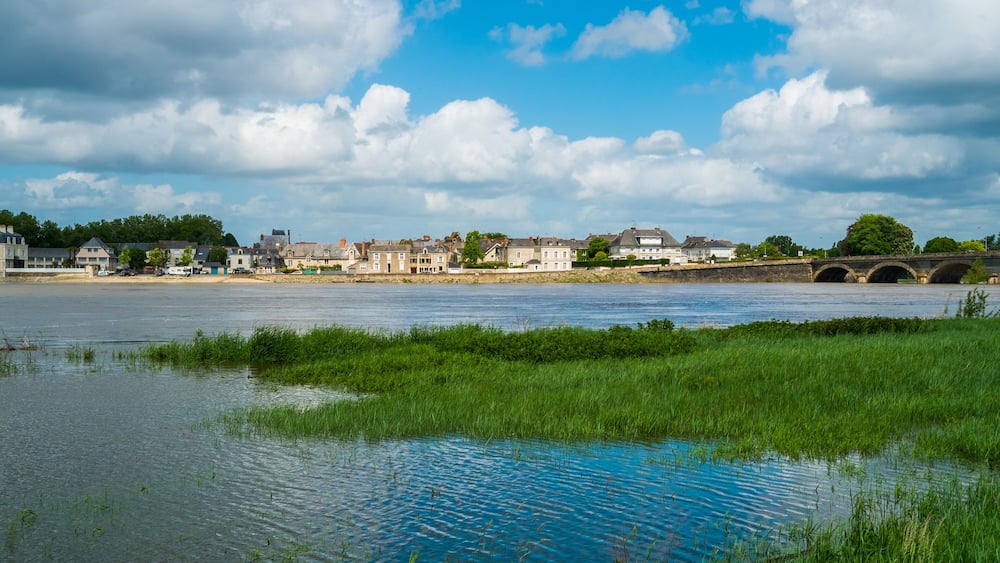 Une rivière avec un pont, des maisons et de la verdure.