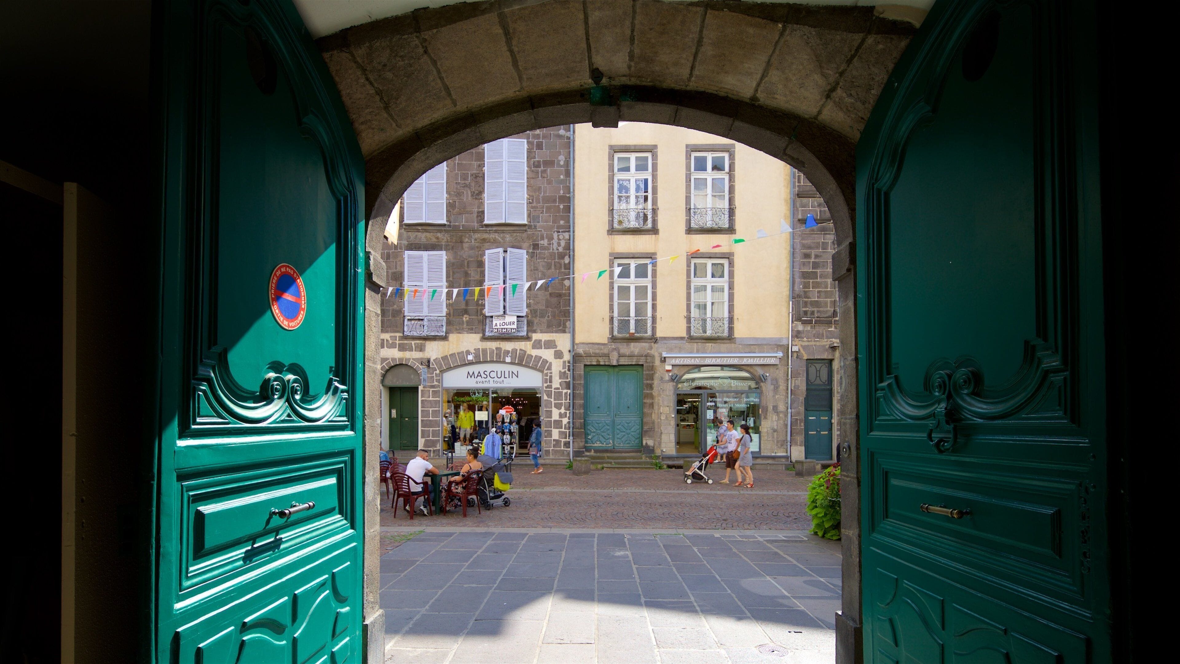 A street view through a green archway with shops and people.
