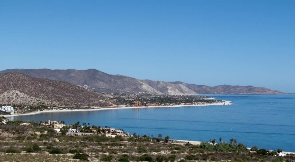 A coastal landscape with a beach, mountains, and a clear blue sky.