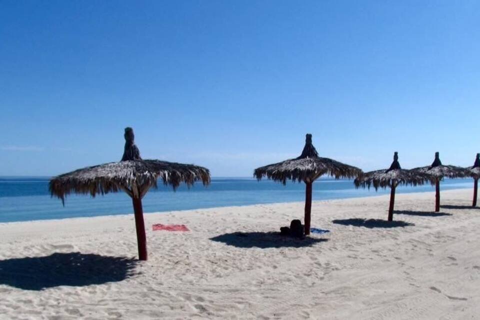 Una playa con sombrillas de paja y un cielo azul despejado.