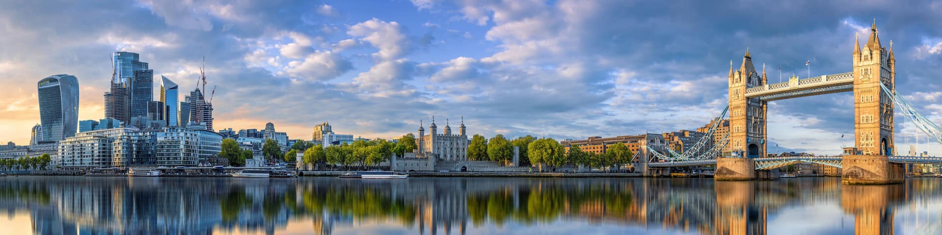 A cityscape with modern skyscrapers, a historic tower bridge, and a calm river reflecting the skyline.