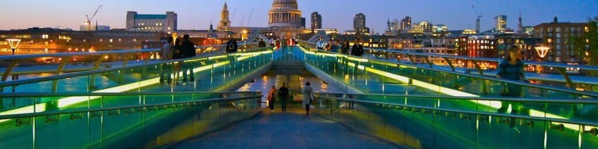 A bridge with glass railings leading to a dome-shaped building in the distance.