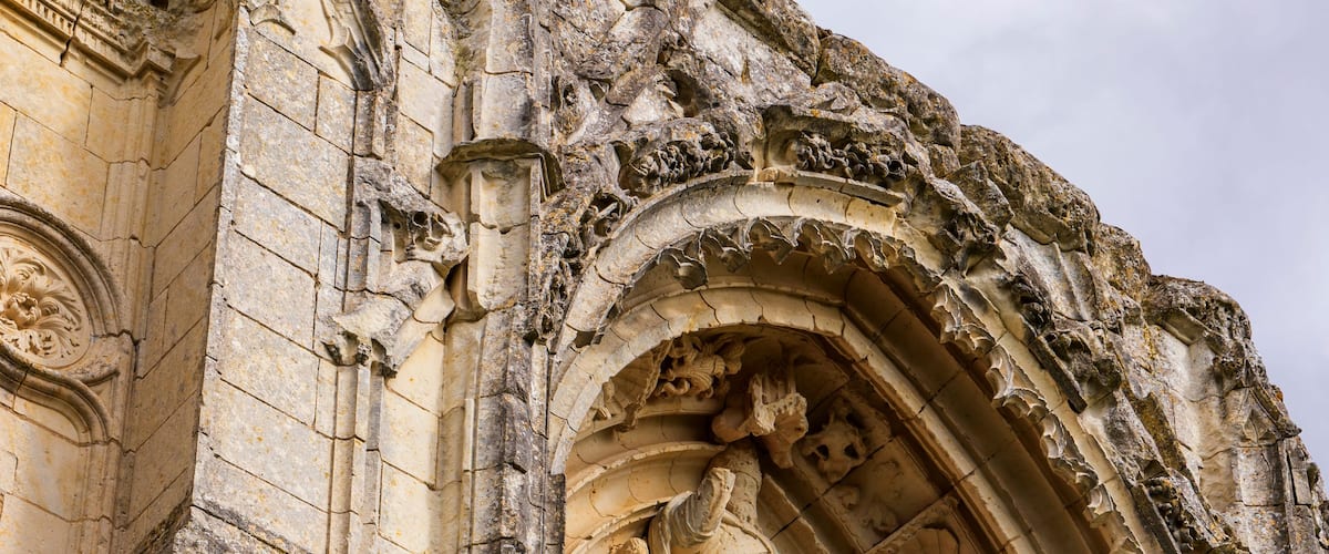 A weathered stone archway with intricate carvings and a circular window.
