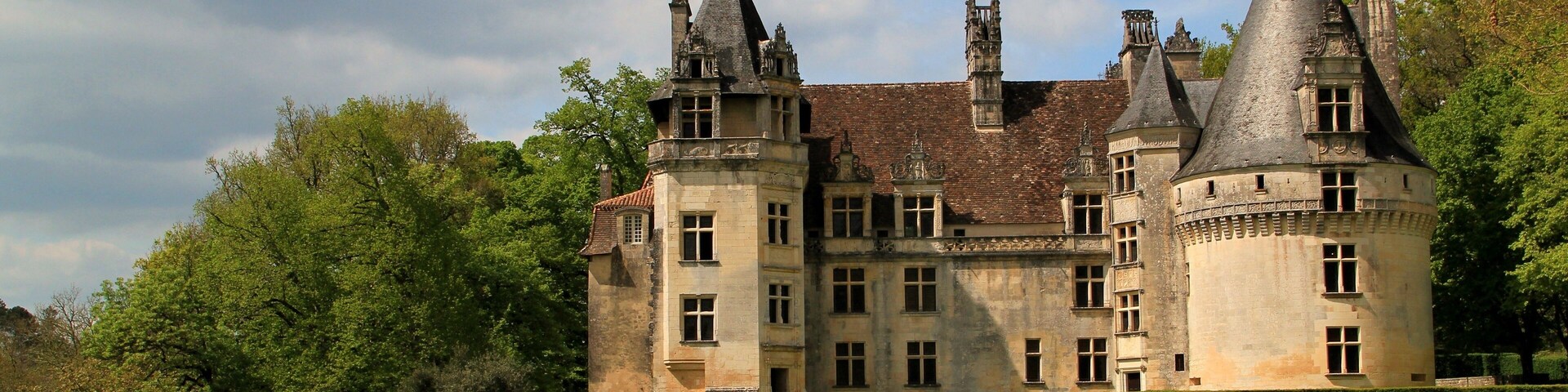 Un castillo histórico con múltiples torres, rodeado de exuberante vegetación y un muro de piedra.