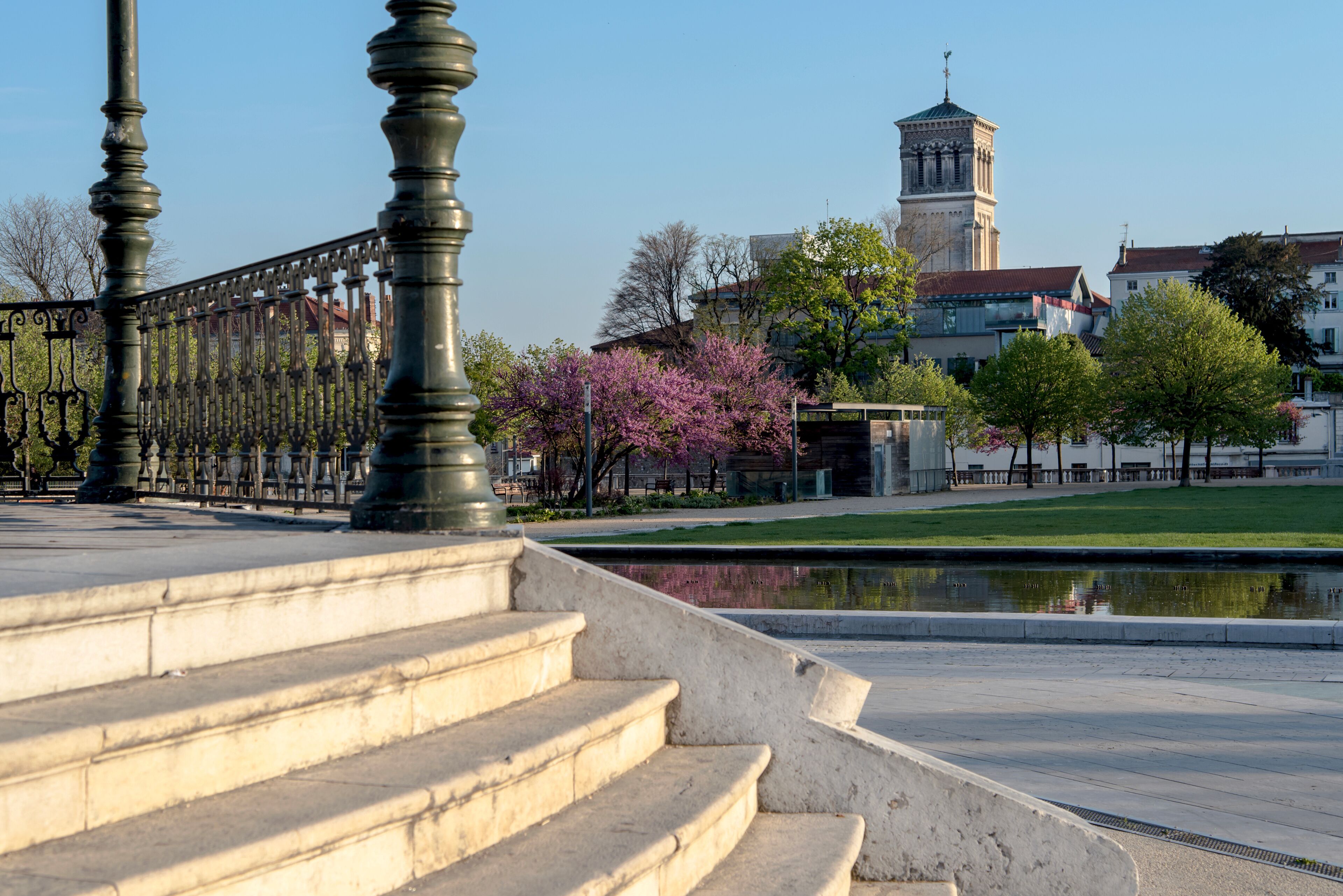 A stone staircase, a metal fence, a pond, and a tower in the background.