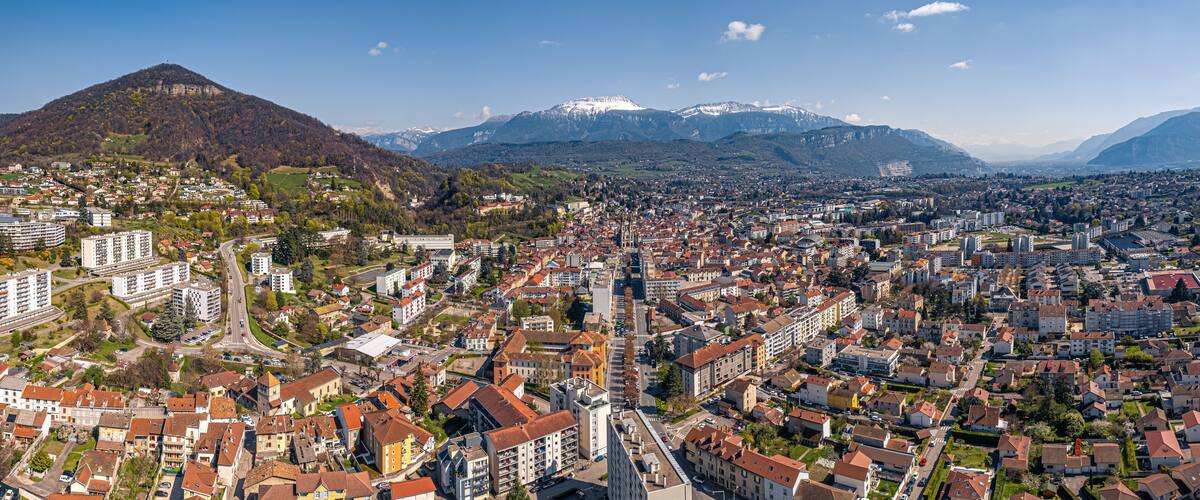 A cityscape with a prominent hill and snow-capped mountains in the background.