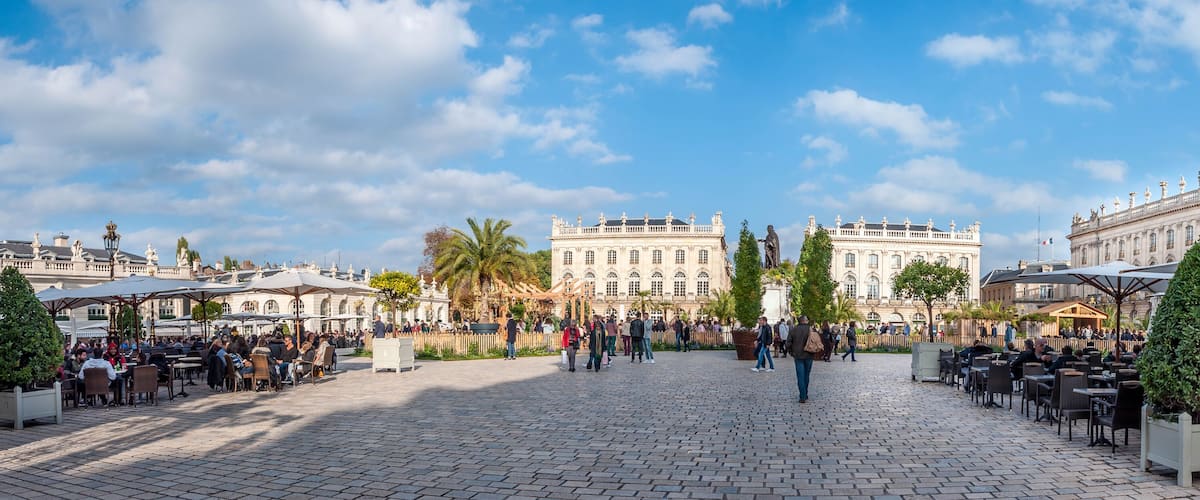 A historic plaza with ornate buildings, cobblestone pavement, and outdoor seating areas.