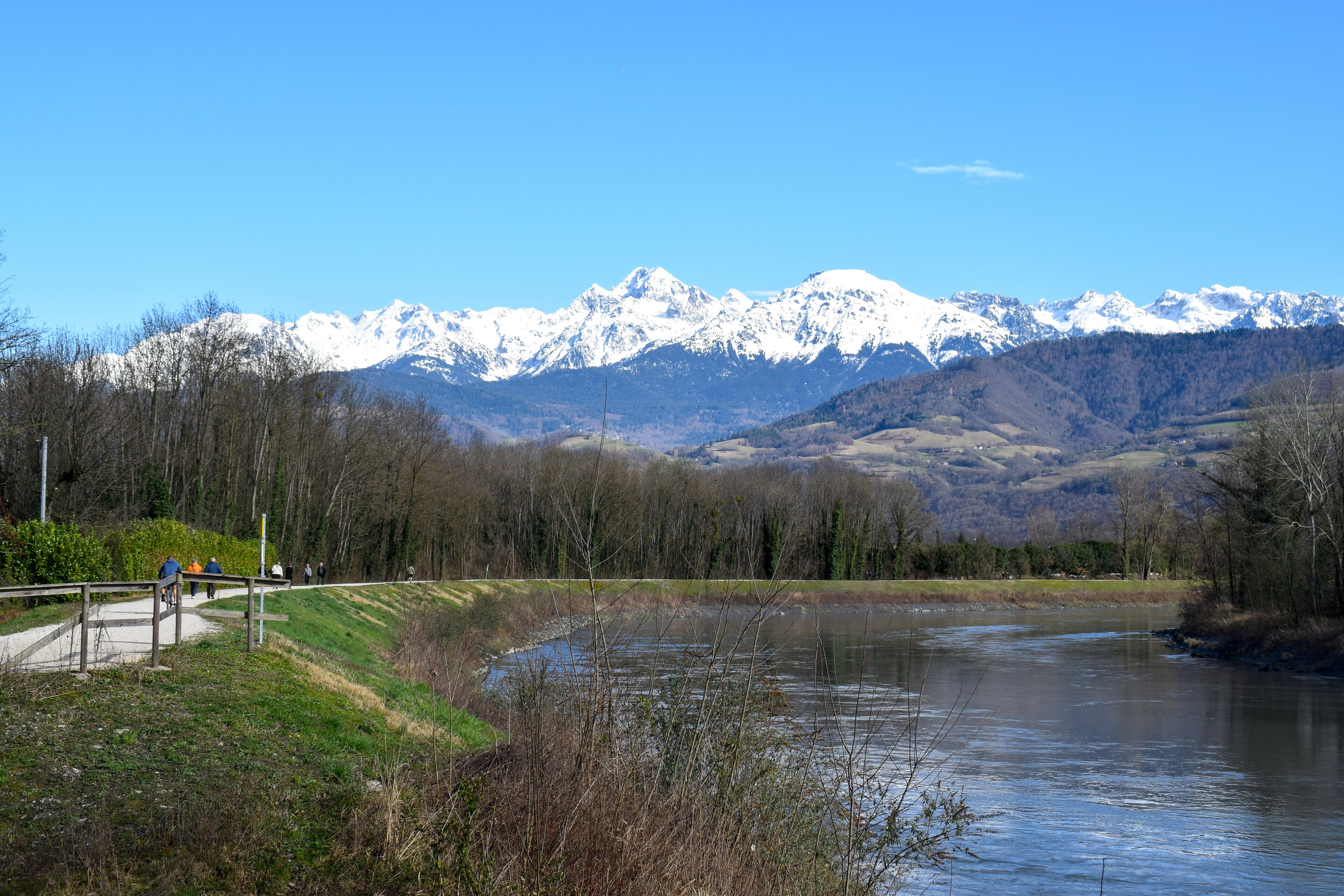 People strolling along the Isere River in Saint-Martin-d&#x27;Heres, with stunning snow-capped Alps in the background. A peaceful mountain landscape.