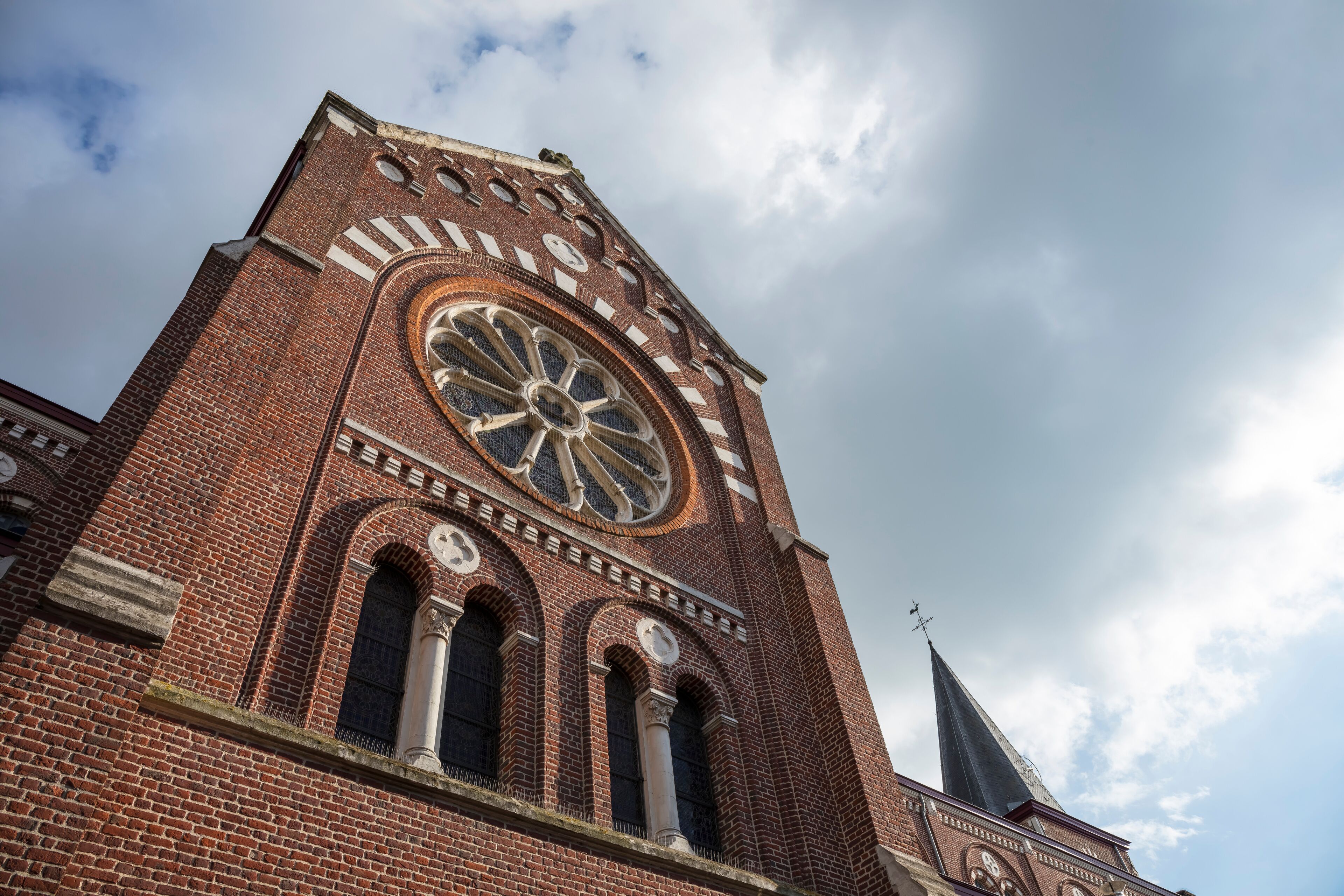 A tall brick church with a large circular window and a spire.