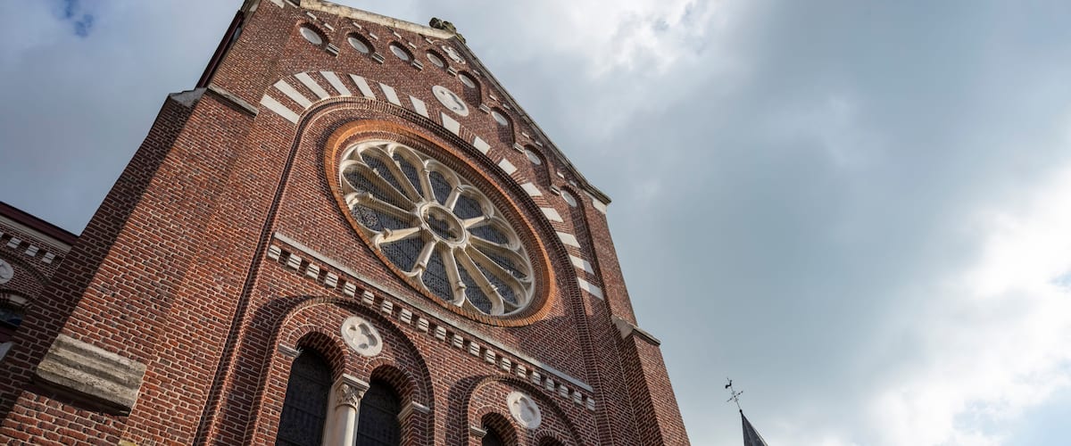A tall brick church with a large circular window and a spire.