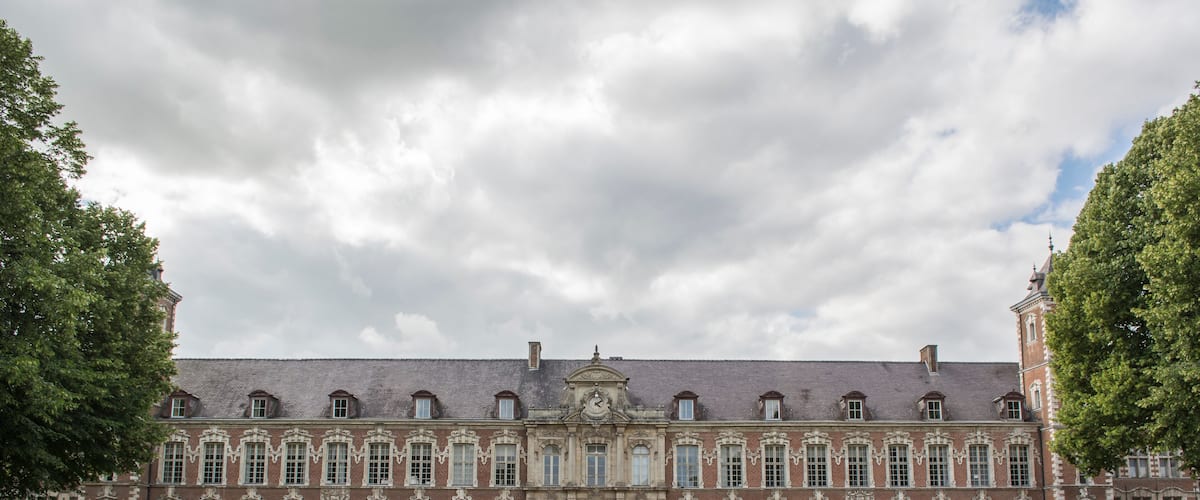 A large, historic building with a symmetrical facade, surrounded by well-manicured gardens and hedges.