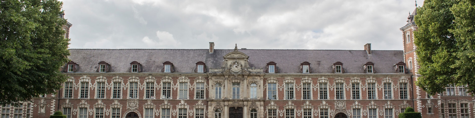 A large, historic building with a symmetrical facade, surrounded by well-manicured gardens and hedges.