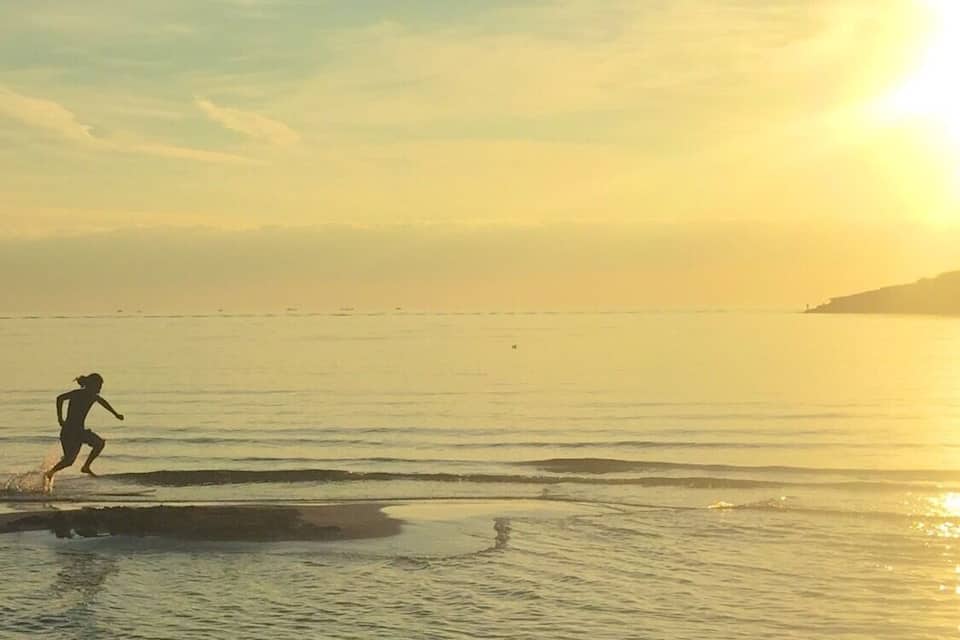 A person running along a beach at sunset with the sun low on the horizon.