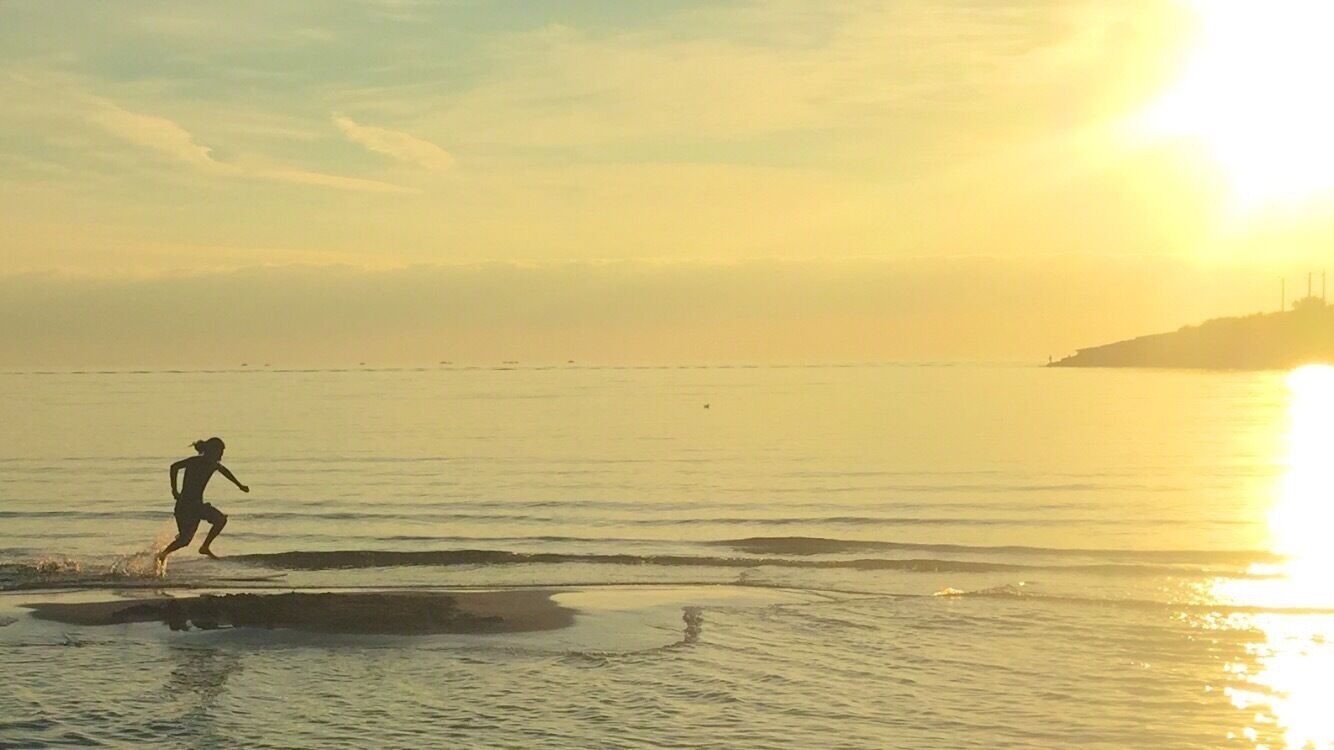 A person running along a beach at sunset with the sun low on the horizon.